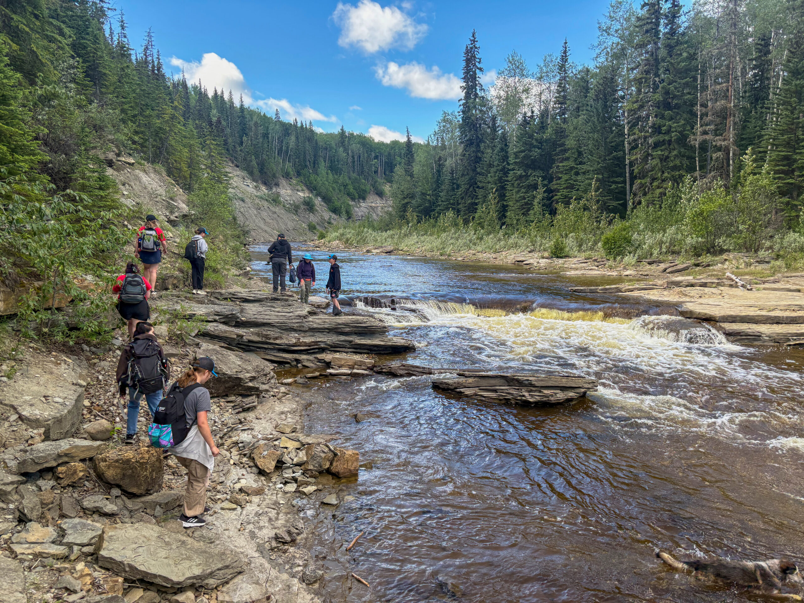 Waterfall in a riverbed with people hiking along the bank